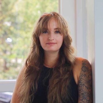 female massage therapist with long curly brown hair, tattoos on left arm