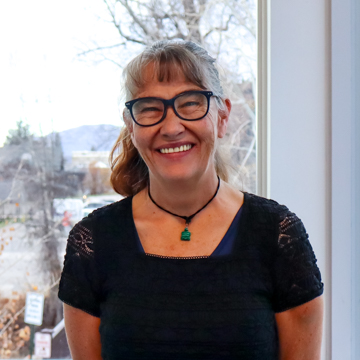 Ann Roberston, massage therapists smiling for headshot in black tshirt in front of a window