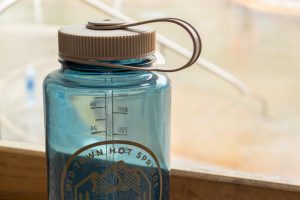Blue reusable water bottle with Old Town Hot Springs logo with the hot spring pools in the background.